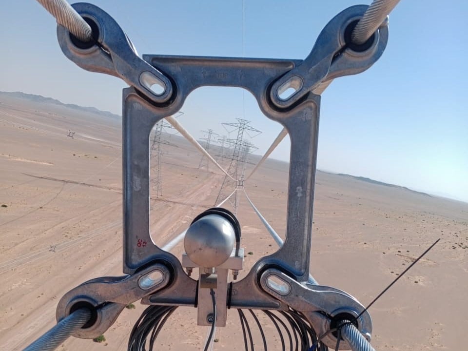 Dämpfungssystem montiert auf Stromleitung für Feldtests in karger Wüstenumgebung mit blauem Himmel.