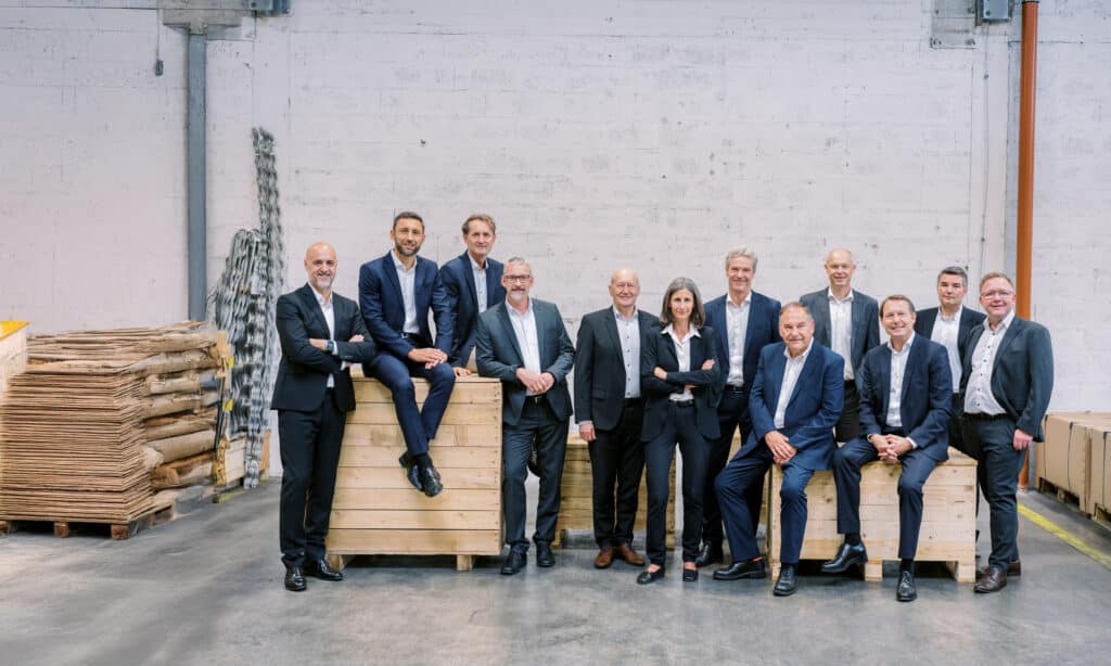 12 Leute des Management-Teams sitzen und stehen auf und um Holzkisten in der Produktionshalle.